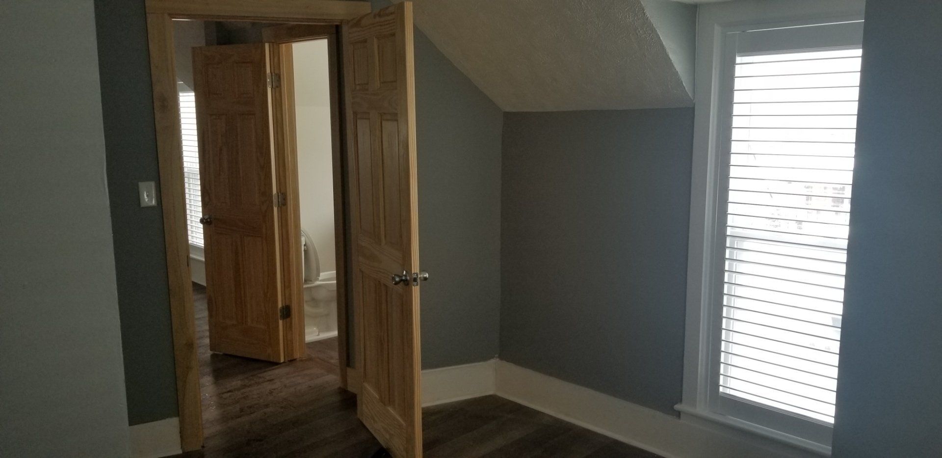 Interior view of a room with open wooden doors, gray walls, and a window with blinds.