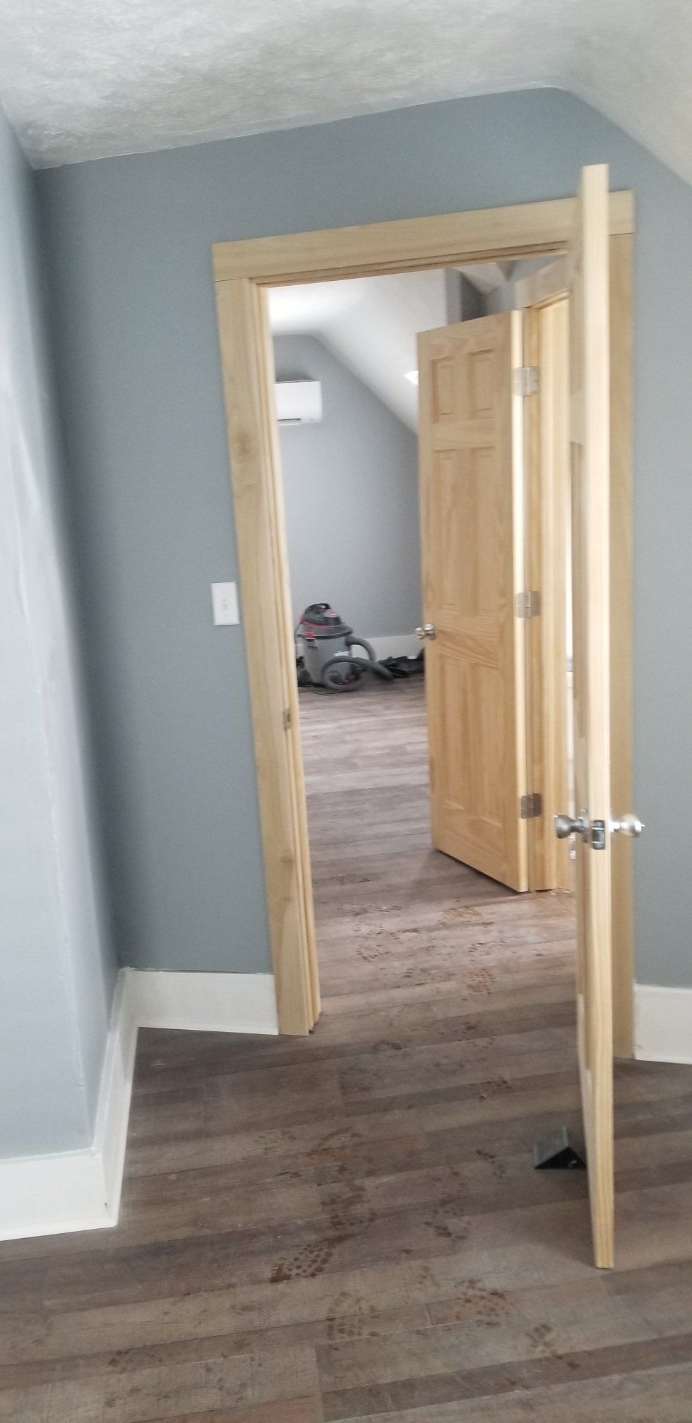 Interior view of a door frame, open door, and hallway with blue walls and wood floors.