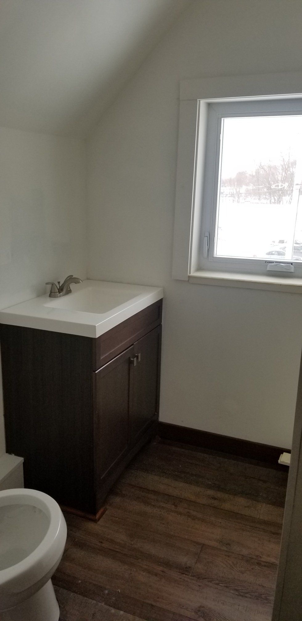Bathroom with dark wooden vanity, white sink, and window. Wood-look flooring.