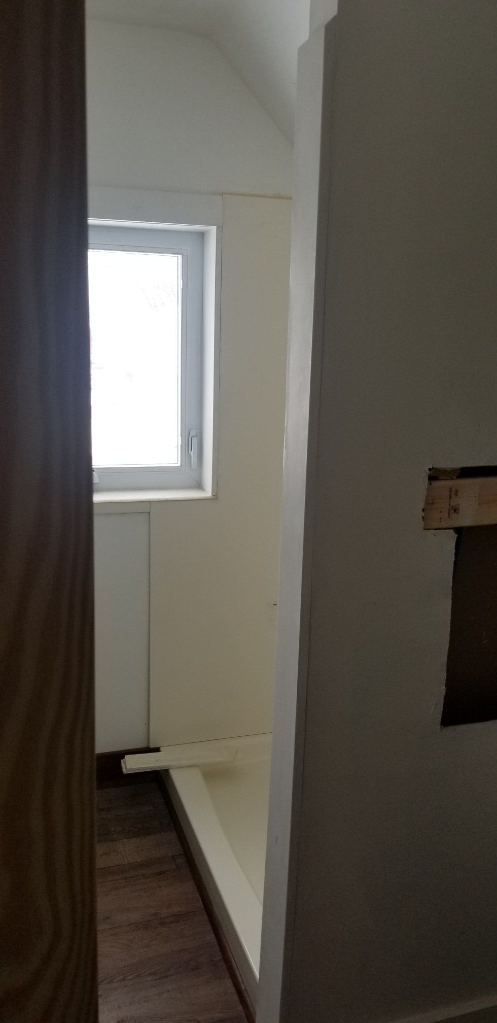 Narrow room with a window at the end. White walls, a wood door frame on the left, and a partially open doorway on the right.