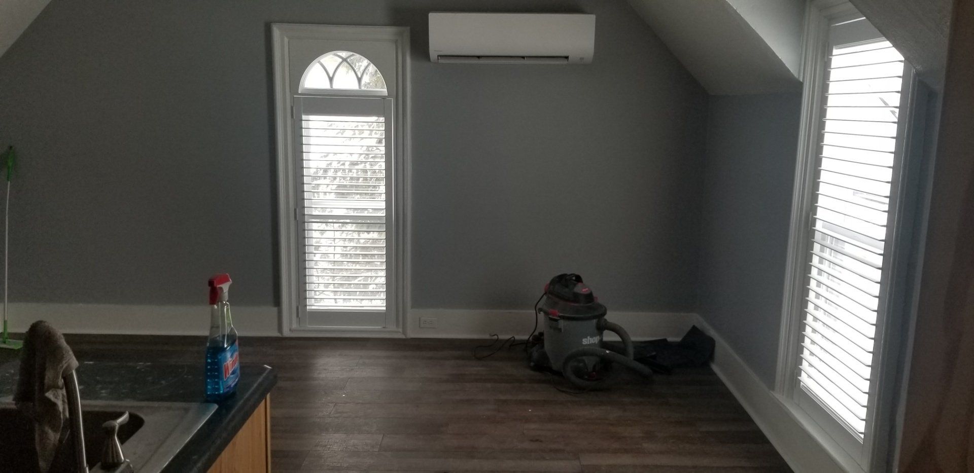A room with gray walls, wood floors, and arched windows. An air conditioner is mounted on the wall.