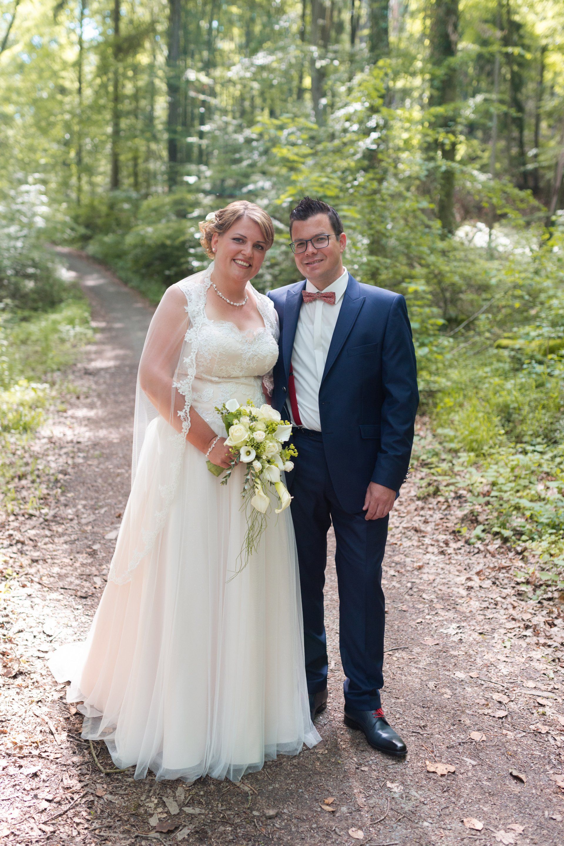 Eine Braut und ein Bräutigam posieren im Wald für ein Foto.