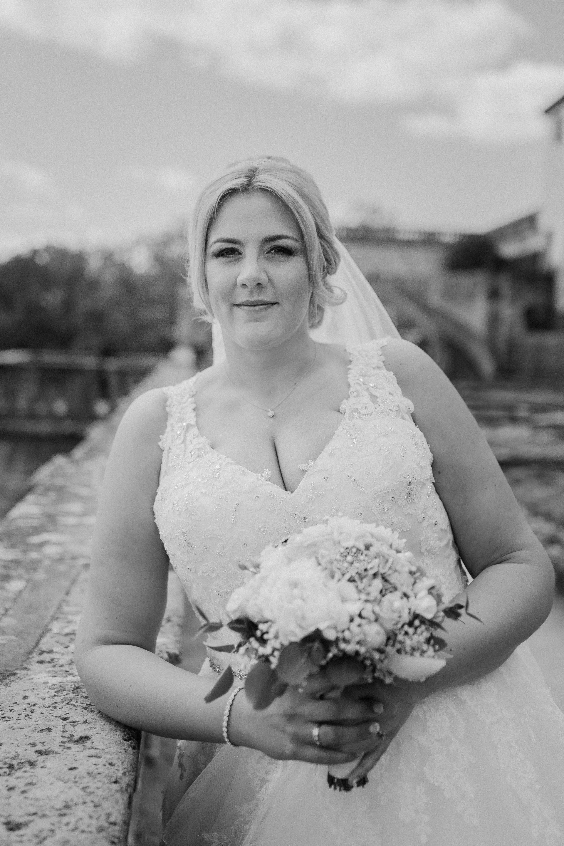 Ein Schwarzweißfoto einer Braut im Brautkleid, die einen Blumenstrauß hält.