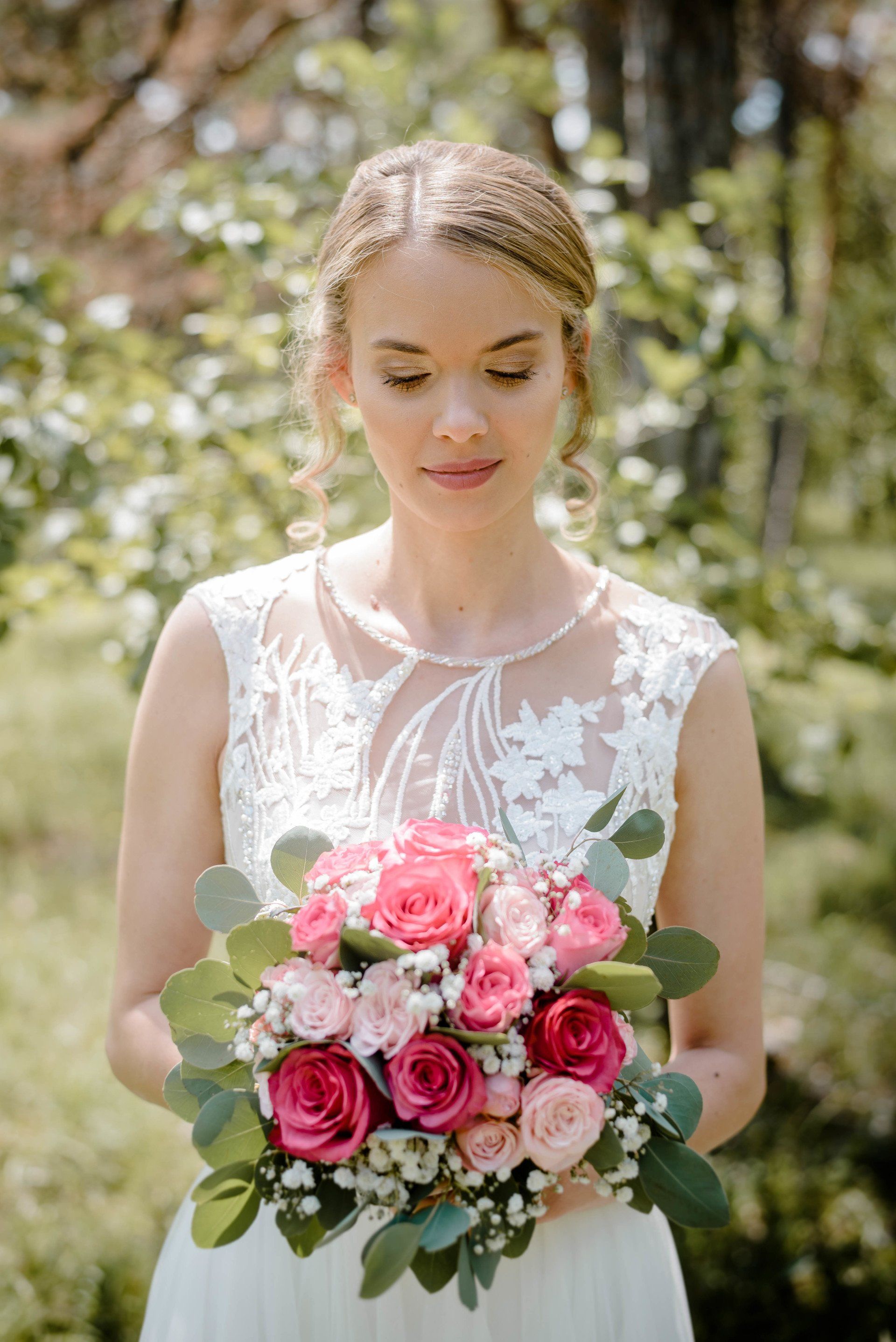 Eine Braut in einem weißen Kleid hält einen Strauß rosa Rosen in der Hand.