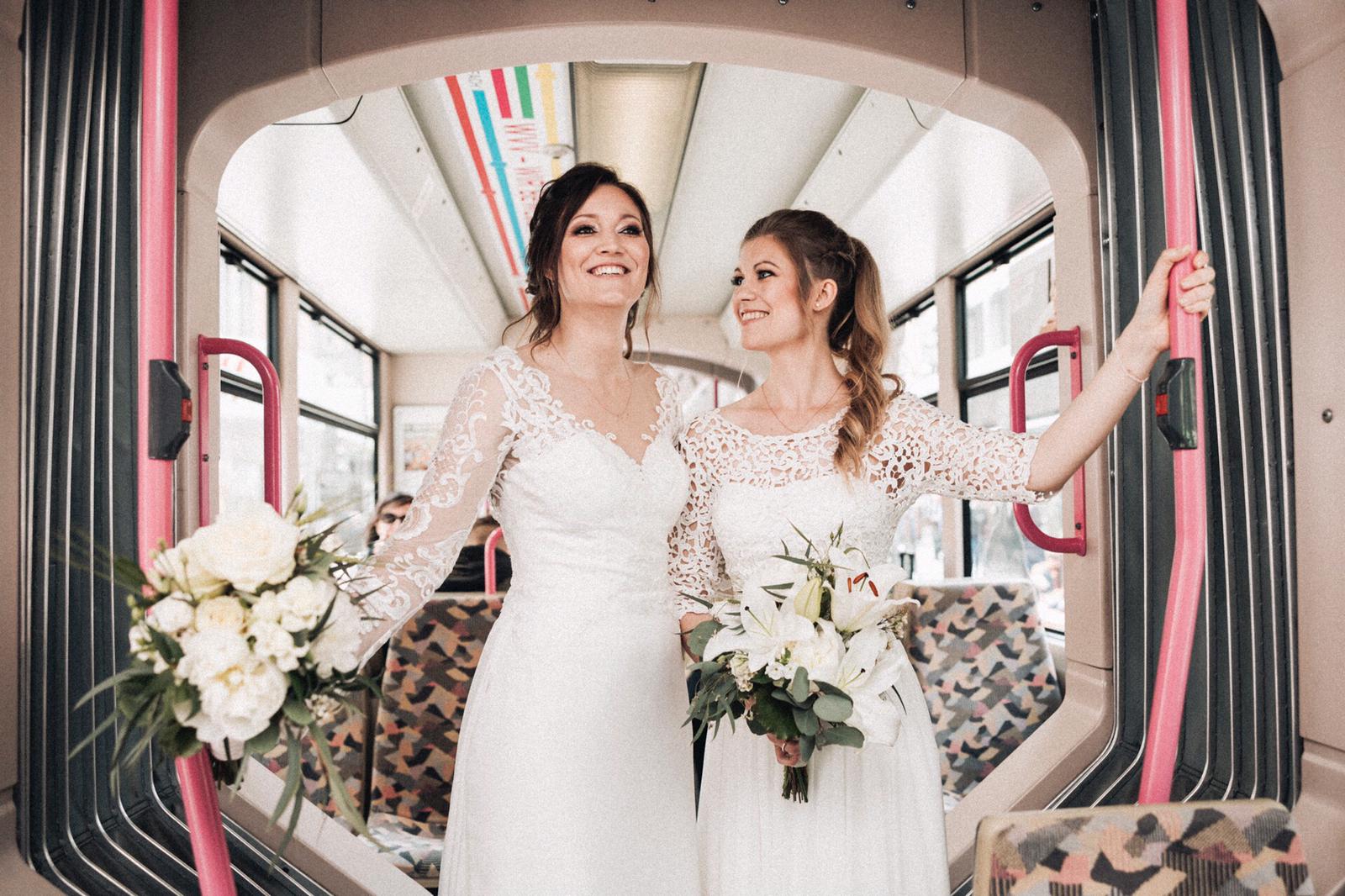 Zwei Frauen in Brautkleidern stehen nebeneinander in einem Bus.