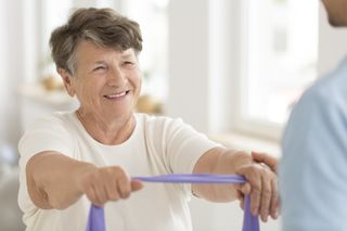 Pphysical Therapy Treatment — Therapist Helping Senior Male To Use Resistance Band in Natick, MA Pphysical Therapy Treatment — Therapist Helping Senior Male To Use Resistance Band in Natick, MA