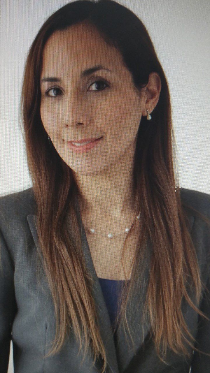 Portrait of a woman with long dark hair in a gray blazer, looking at the camera with a slight smile