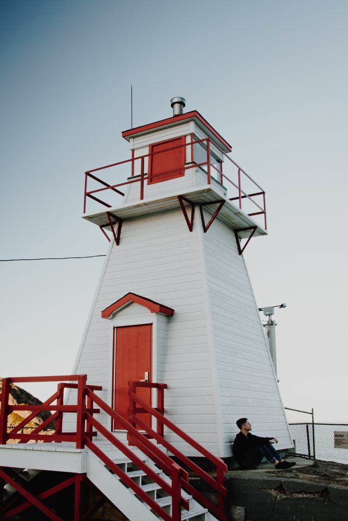 White lighthouse with red trim and stairs, viewed from below against a pale sky.
