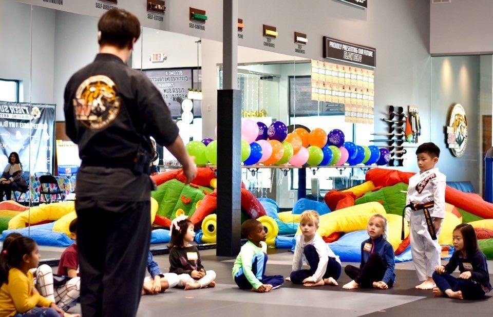 A man is standing in front of a group of children sitting on the floor.