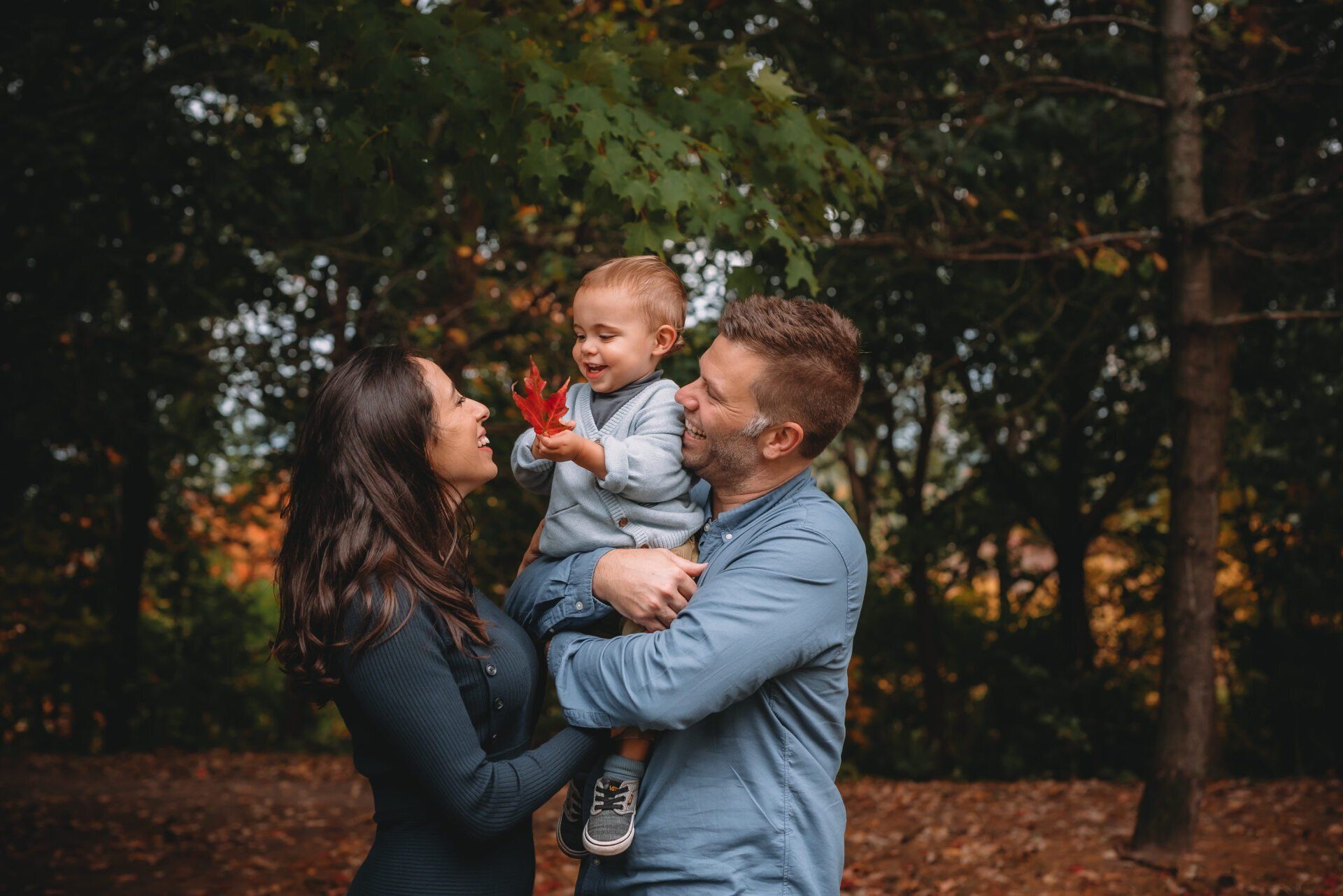 Photo of mom embracing dad holding baby while standing in a field for family photography