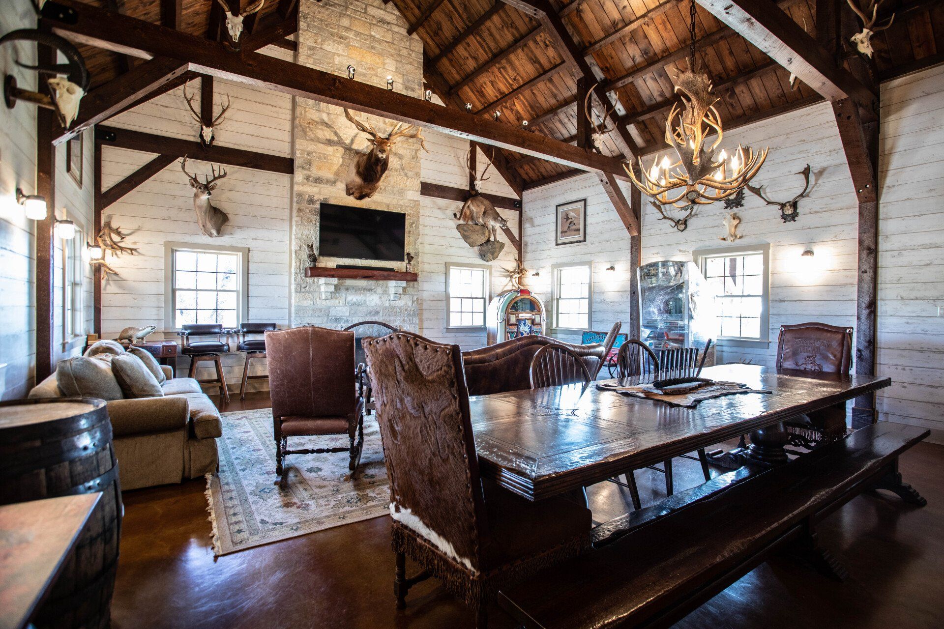 Rustic lodge interior with a large wooden table, antler chandelier, and taxidermy.