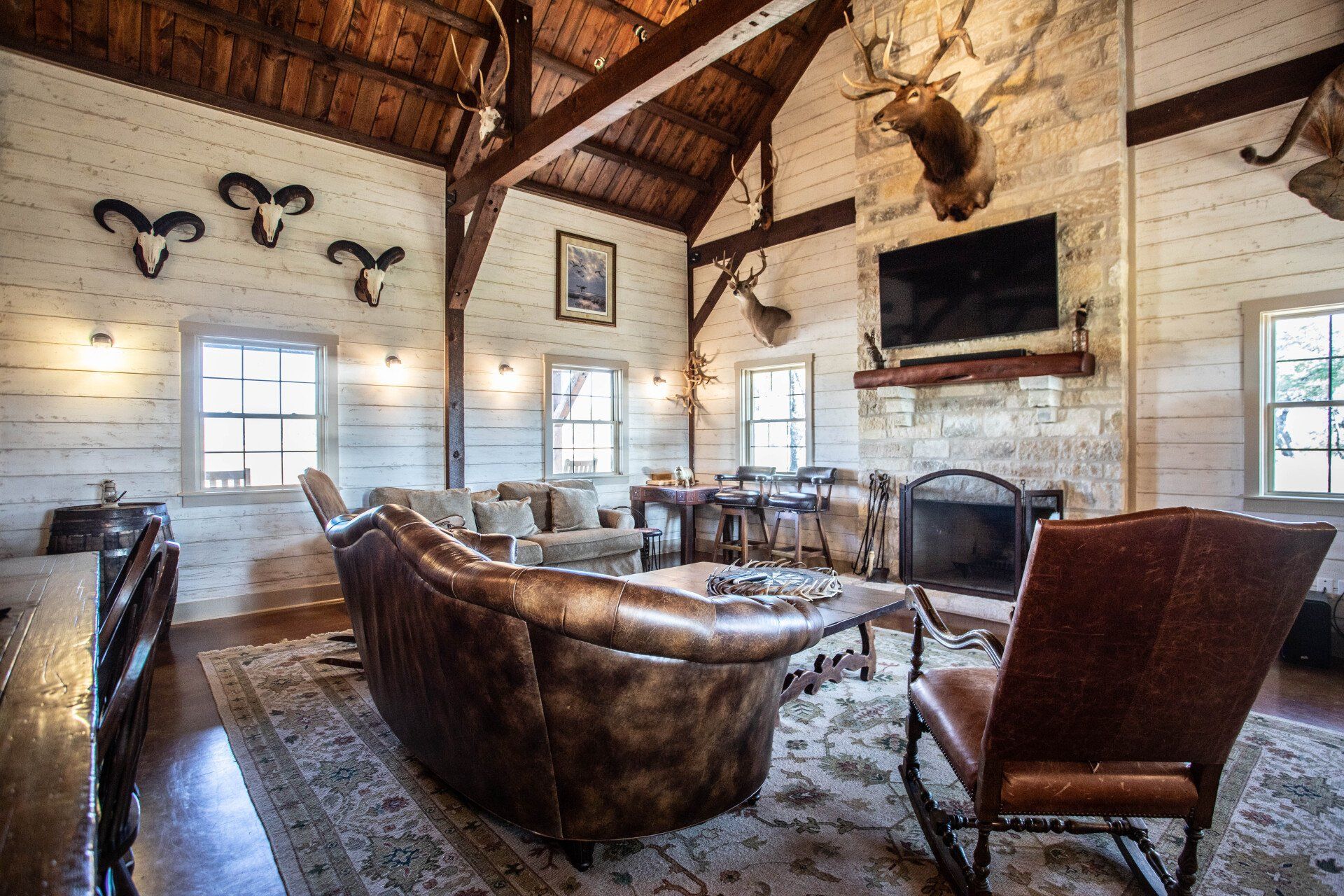 Rustic living room with taxidermy, fireplace, leather furniture, and exposed beams.