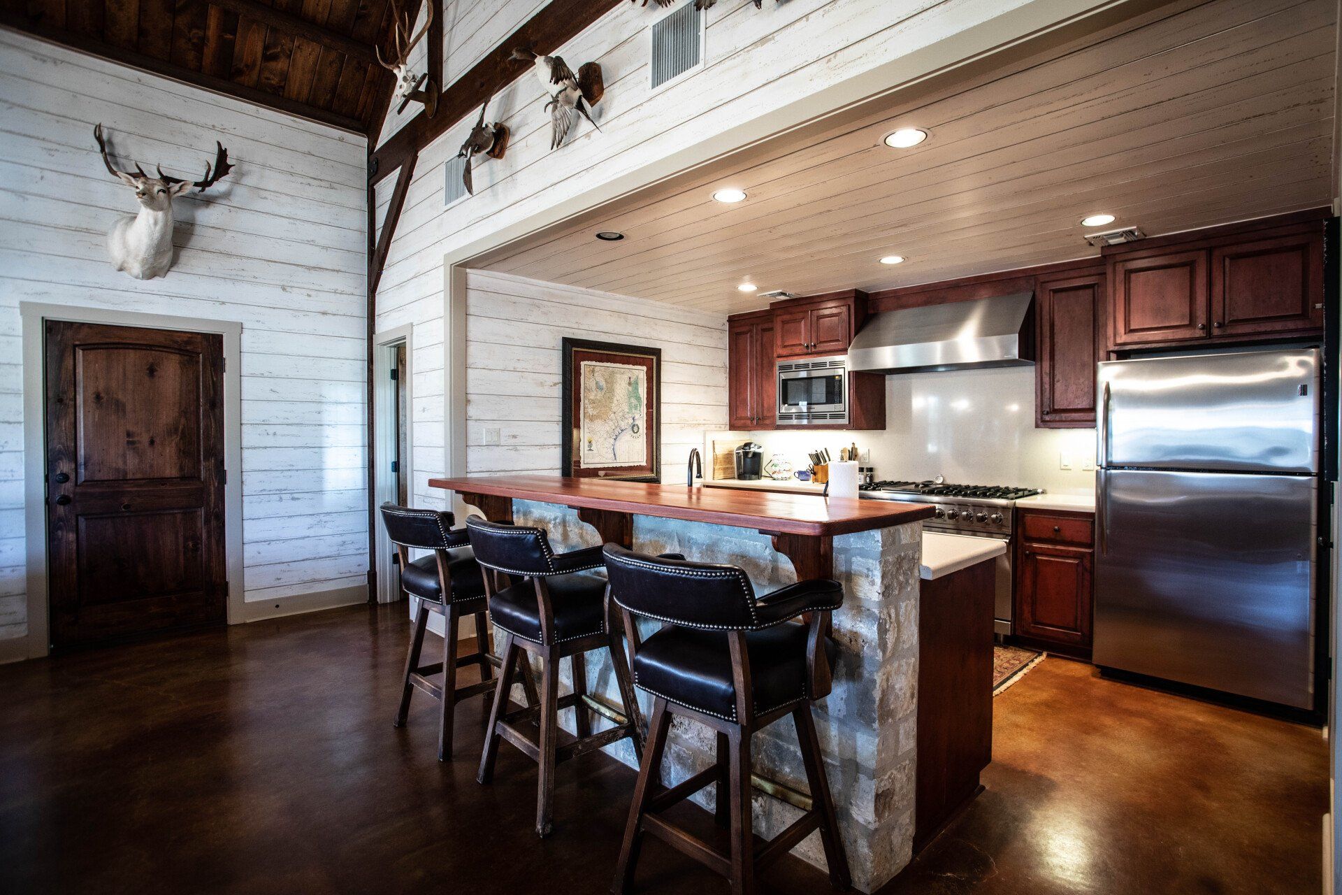 Kitchen with a rustic design: island with stools, wooden cabinetry, stainless steel appliances, animal mounts.
