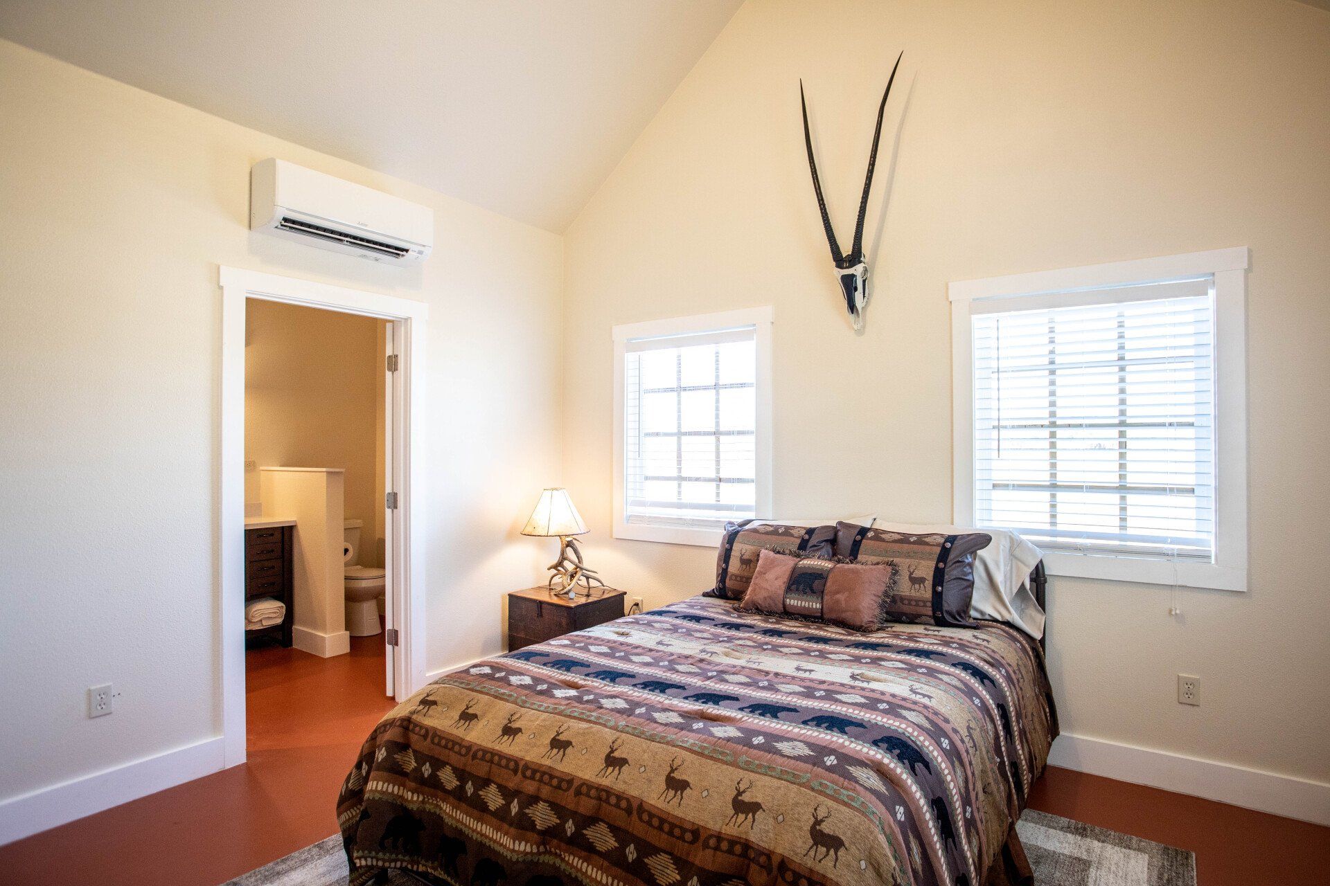 Bedroom with bed, two windows, antelope skull art, and an open door to a bathroom.