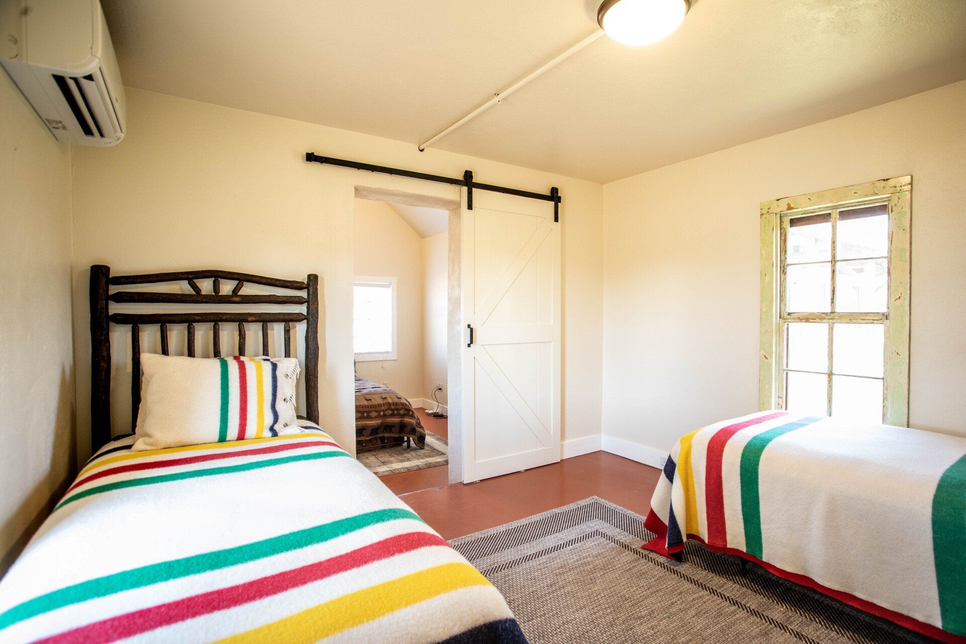 Two twin beds with colorful striped blankets in a bedroom with a barn door.