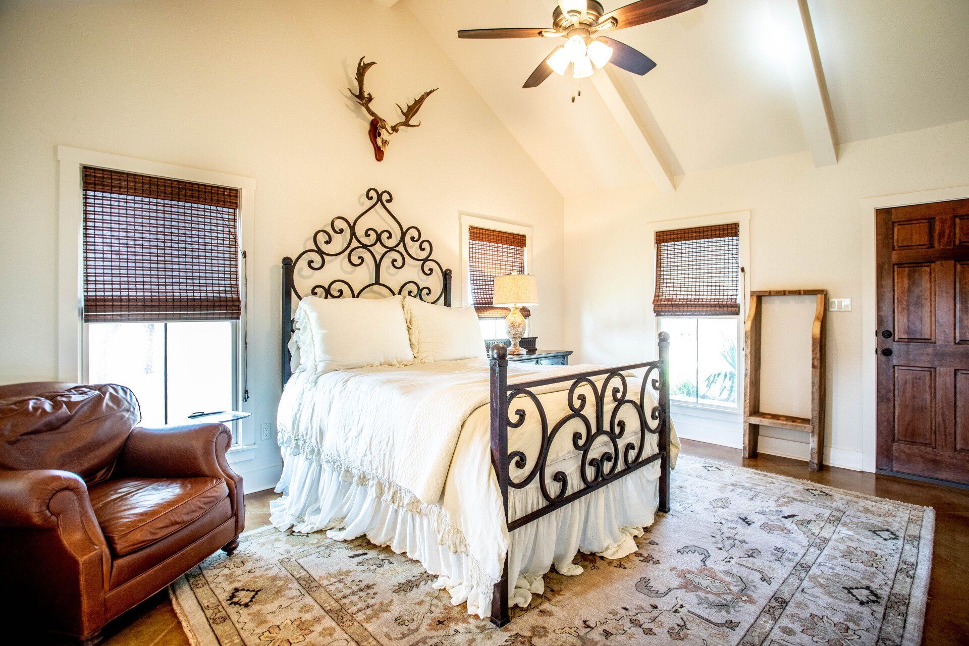 Bedroom with ornate bed, leather chair, rug, wood door, and deer antlers on the wall.