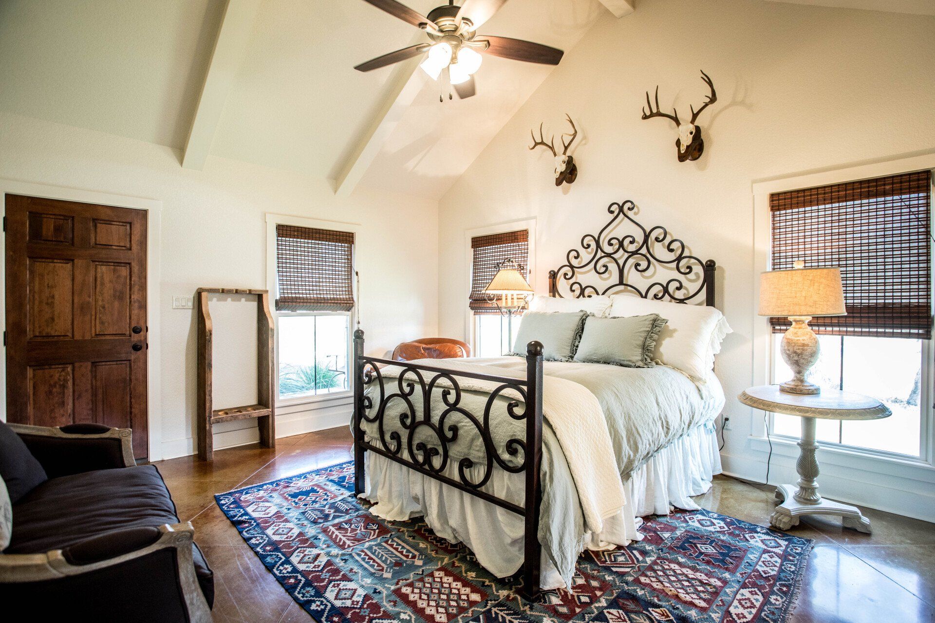Bedroom with wrought iron bed, rug, antlers, and brown door.