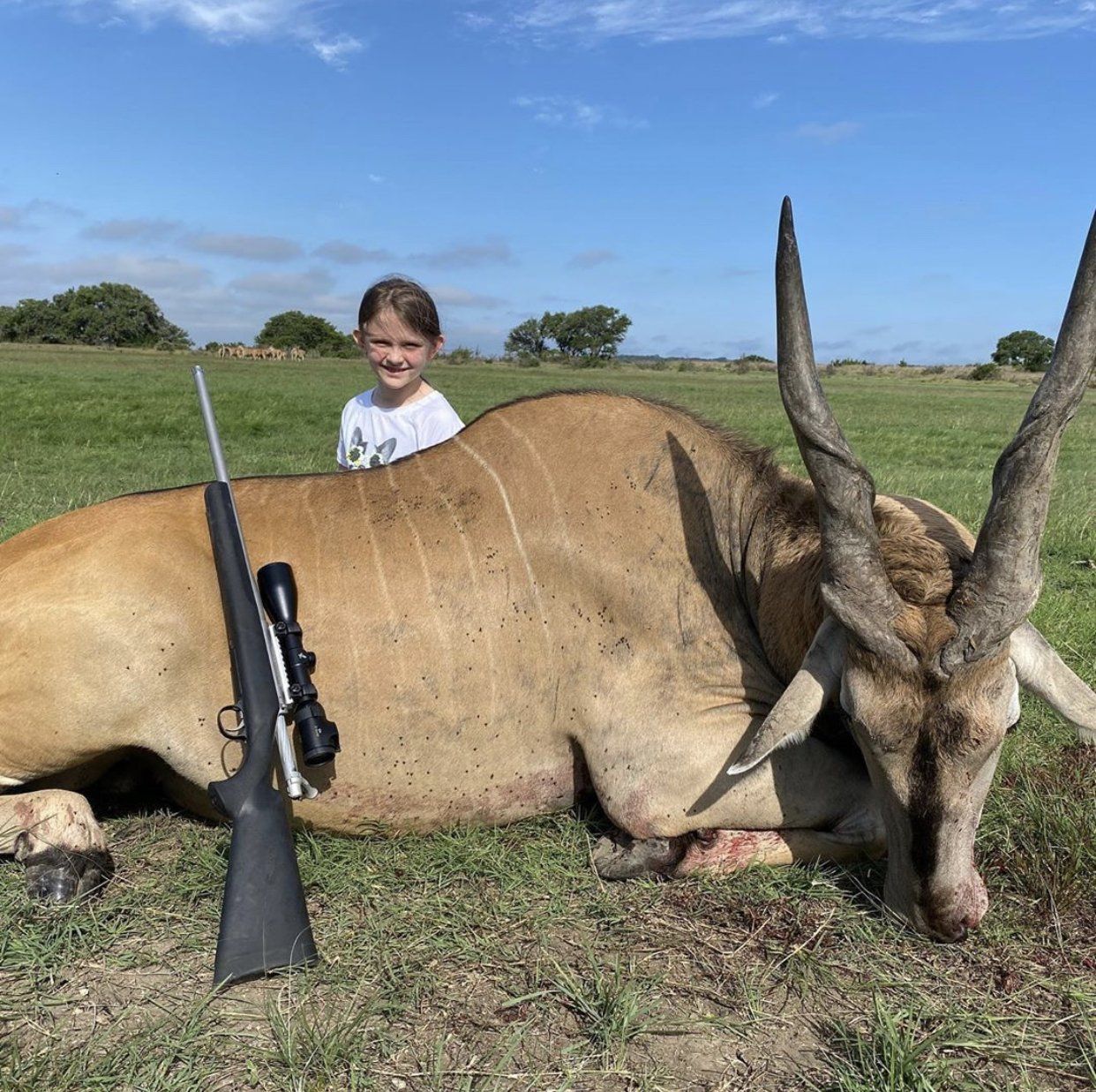 Young girl with large antelope and rifle on grassy field.