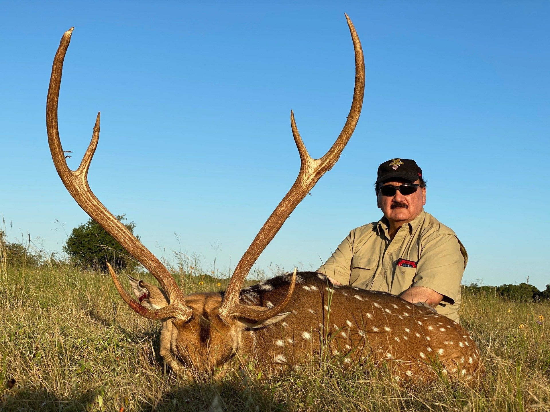Man poses with spotted deer he hunted outdoors, sunny day.