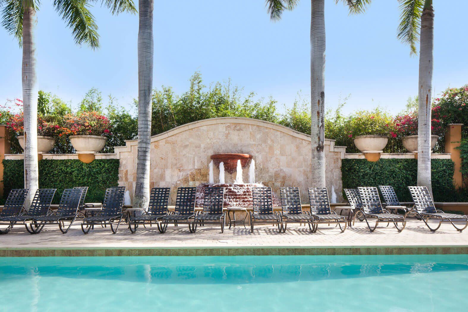 Resort poolside lounge with palm trees, chairs, and stone cabana behind turquoise water