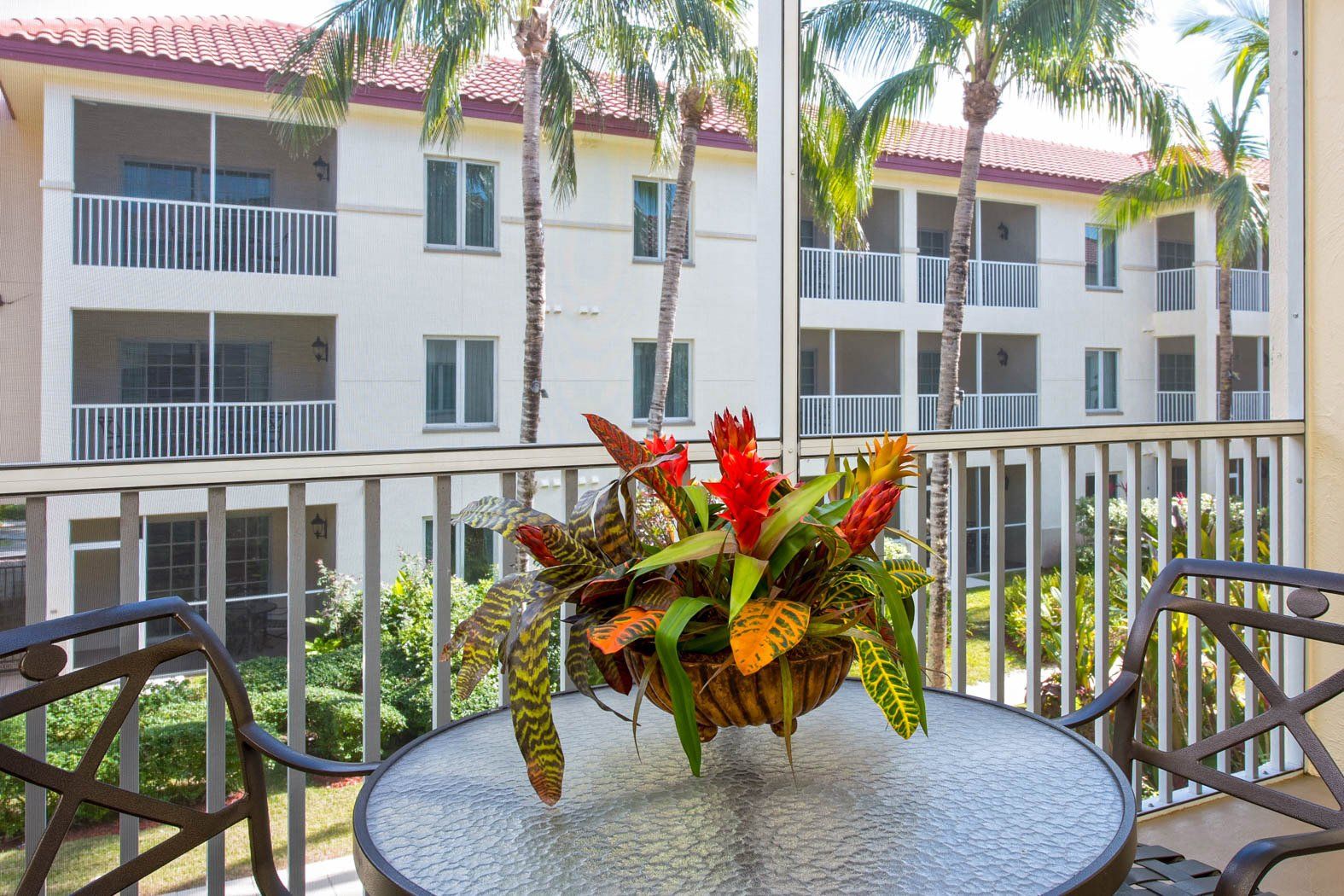 Patio table with tropical flower arrangement overlooking apartment balconies and palm trees