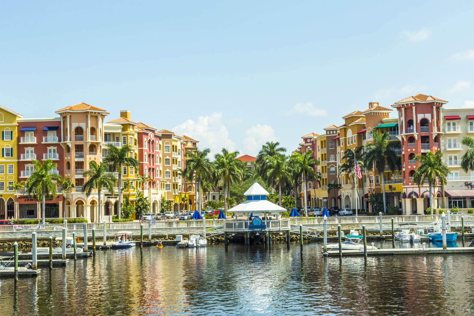 Colorful waterfront apartments and marina with sailboats reflected in calm water under a blue sky