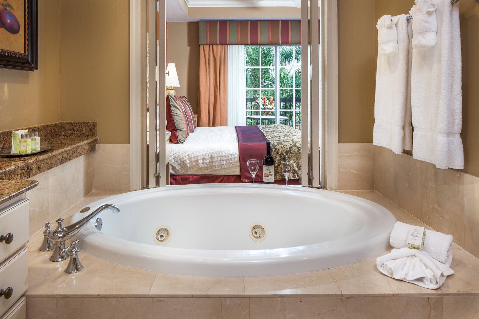 Bathroom with a large oval soaking tub, towels, and a view into a bedroom through an open doorway.