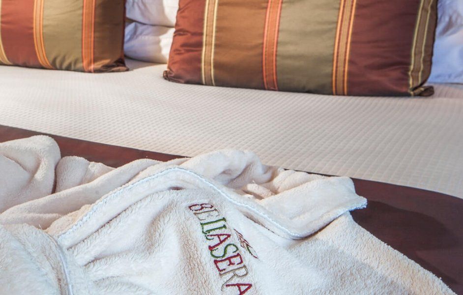White embroidered bathrobe on a bed with striped pillows and a light-colored coverlet