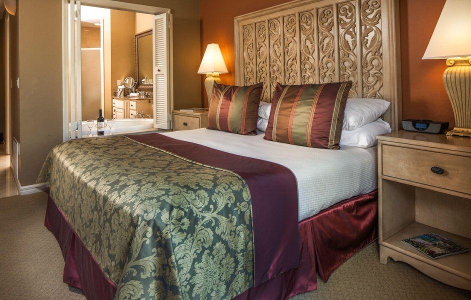 Elegant hotel bedroom with patterned bedspread, bedside lamp, and open doorway to a bathroom