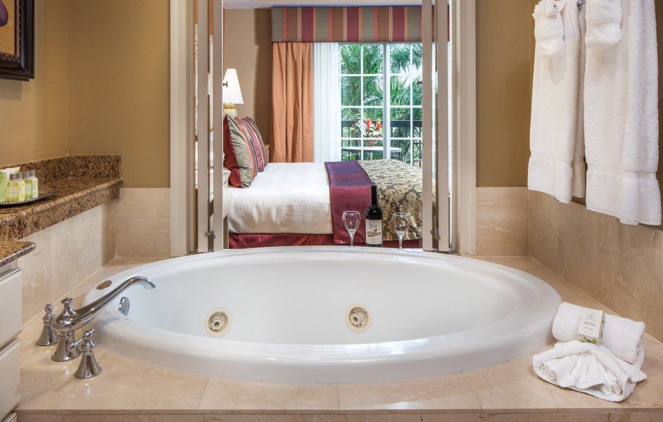 Bathroom with a corner soaking tub, towels, and a view into a bedroom with a bed and window.