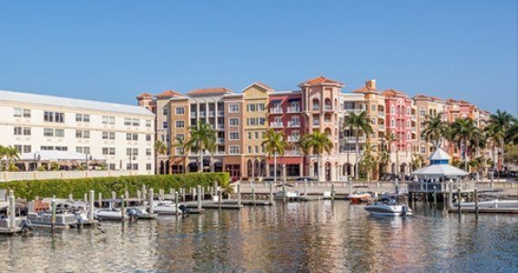 Waterfront marina with colorful apartment buildings, docked boats, and calm water under a clear blue sky.