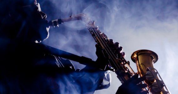 Silhouetted saxophonist playing under blue stage lights and smoke