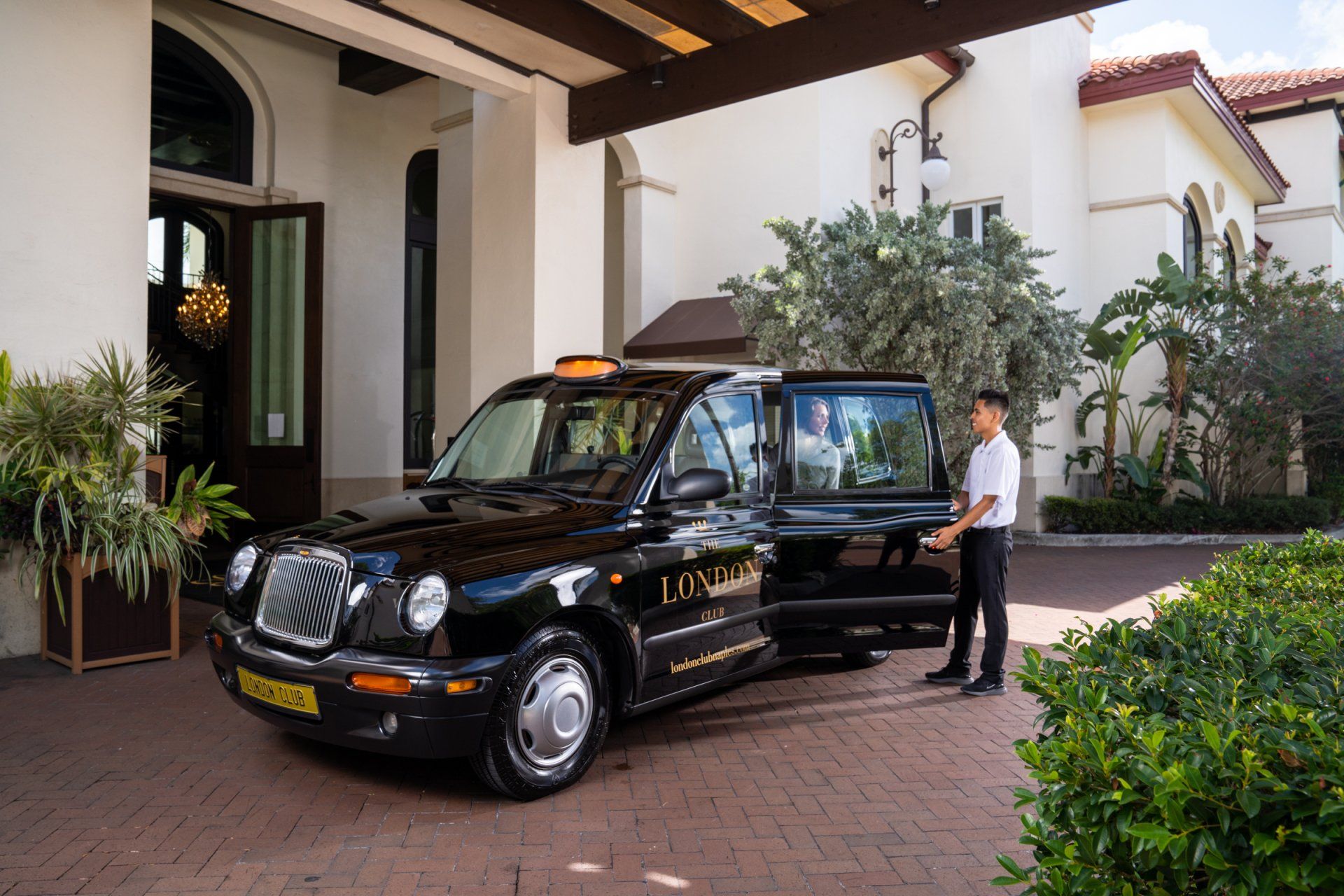 Black taxi pulling up at a building entrance, with a driver standing beside the open door.