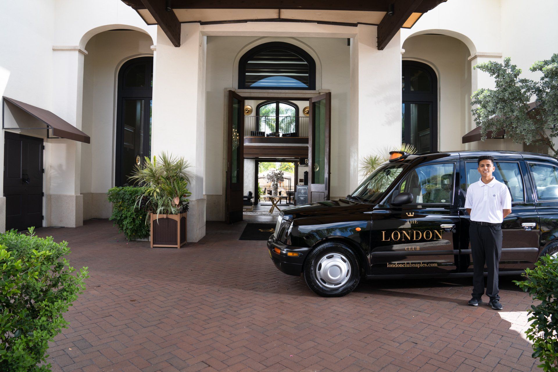 Black taxi parked at a hotel entrance, with a driver standing beside it.