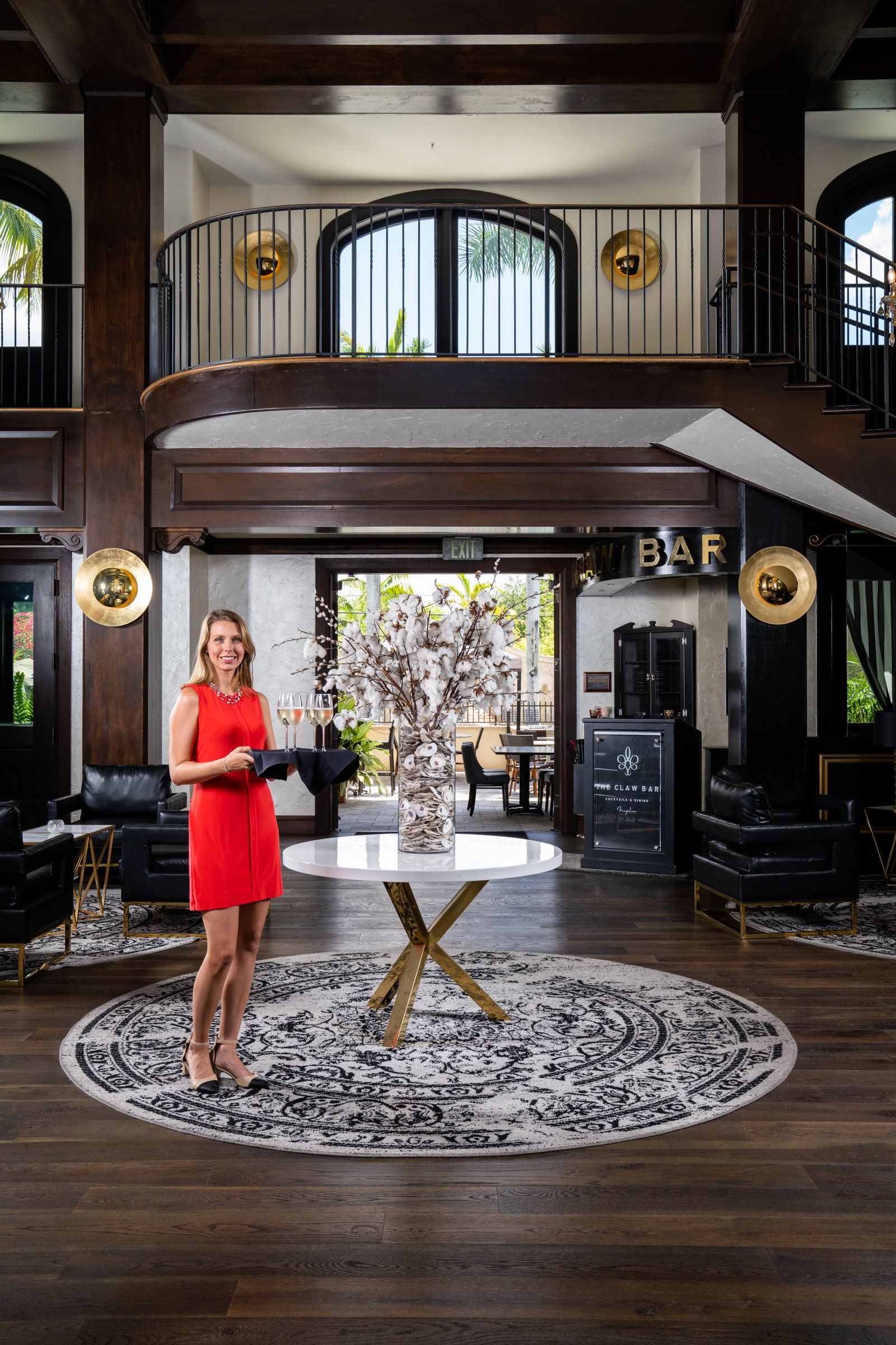 Woman in a red dress standing in a grand lobby with a staircase, fireplace, and patterned rug.