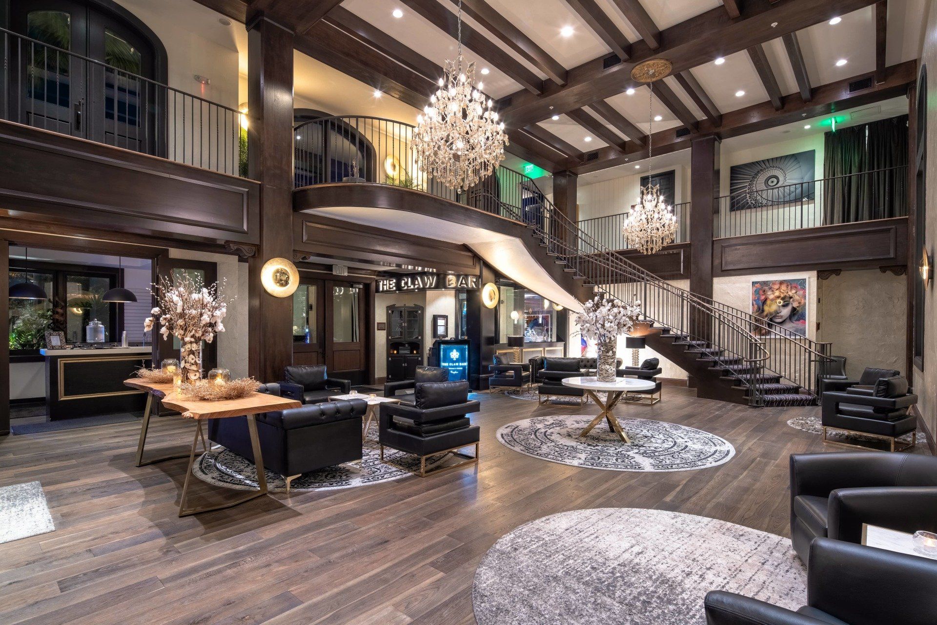 Luxurious hotel lobby with chandeliers, black seating, and a grand staircase in warm lighting