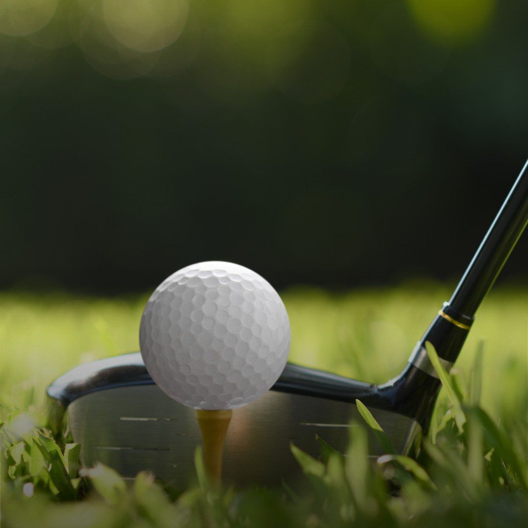 Golf ball on tee in front of a club on a grassy course, with a blurred green background