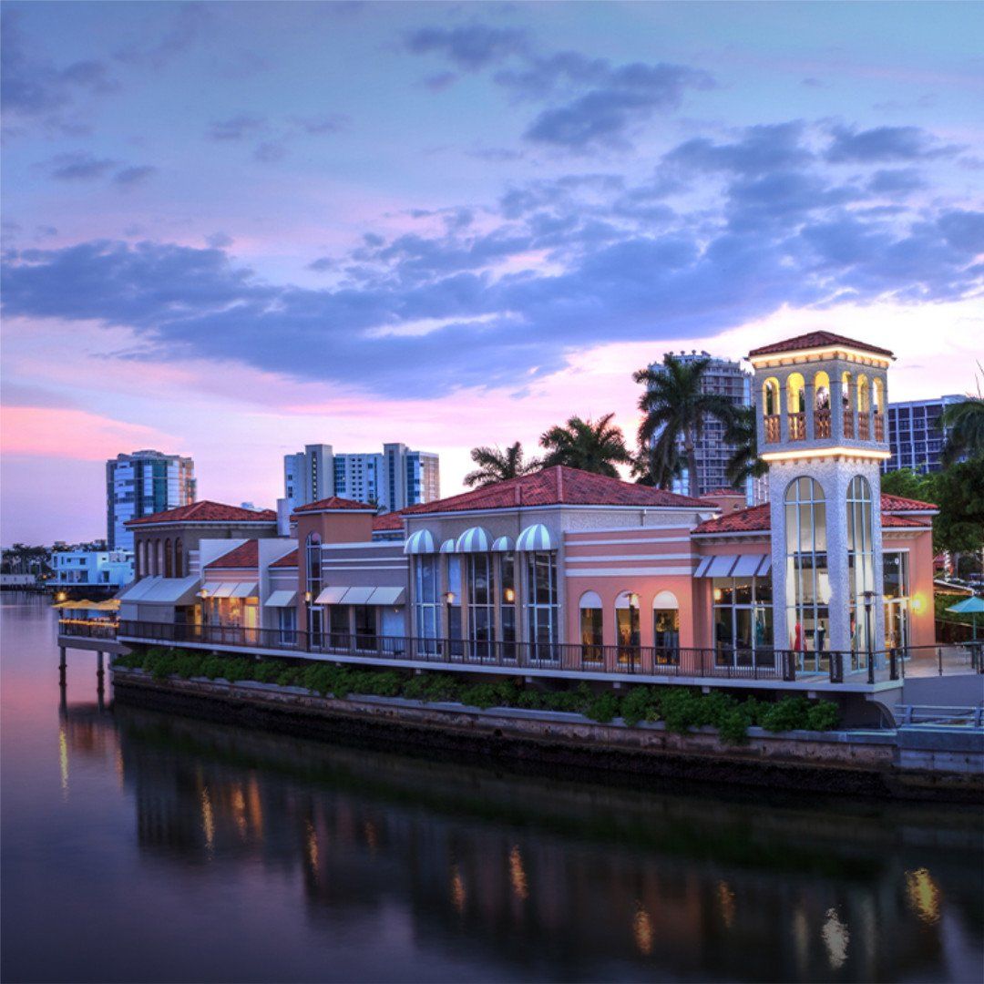 Riverside promenade at dusk with pastel sky, lit buildings, and calm water reflections