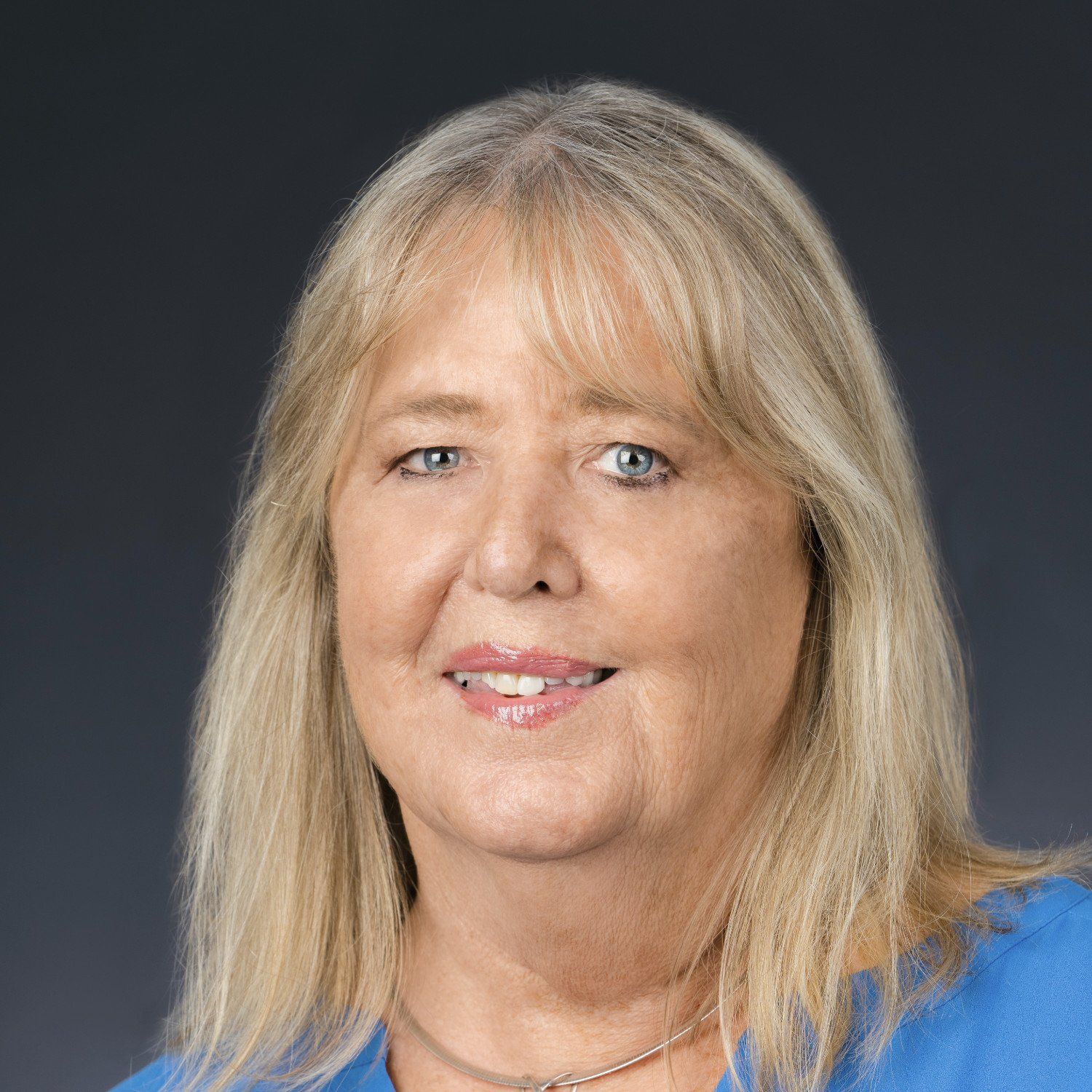 Portrait of a smiling person with blonde hair against a dark background, wearing a blue top.