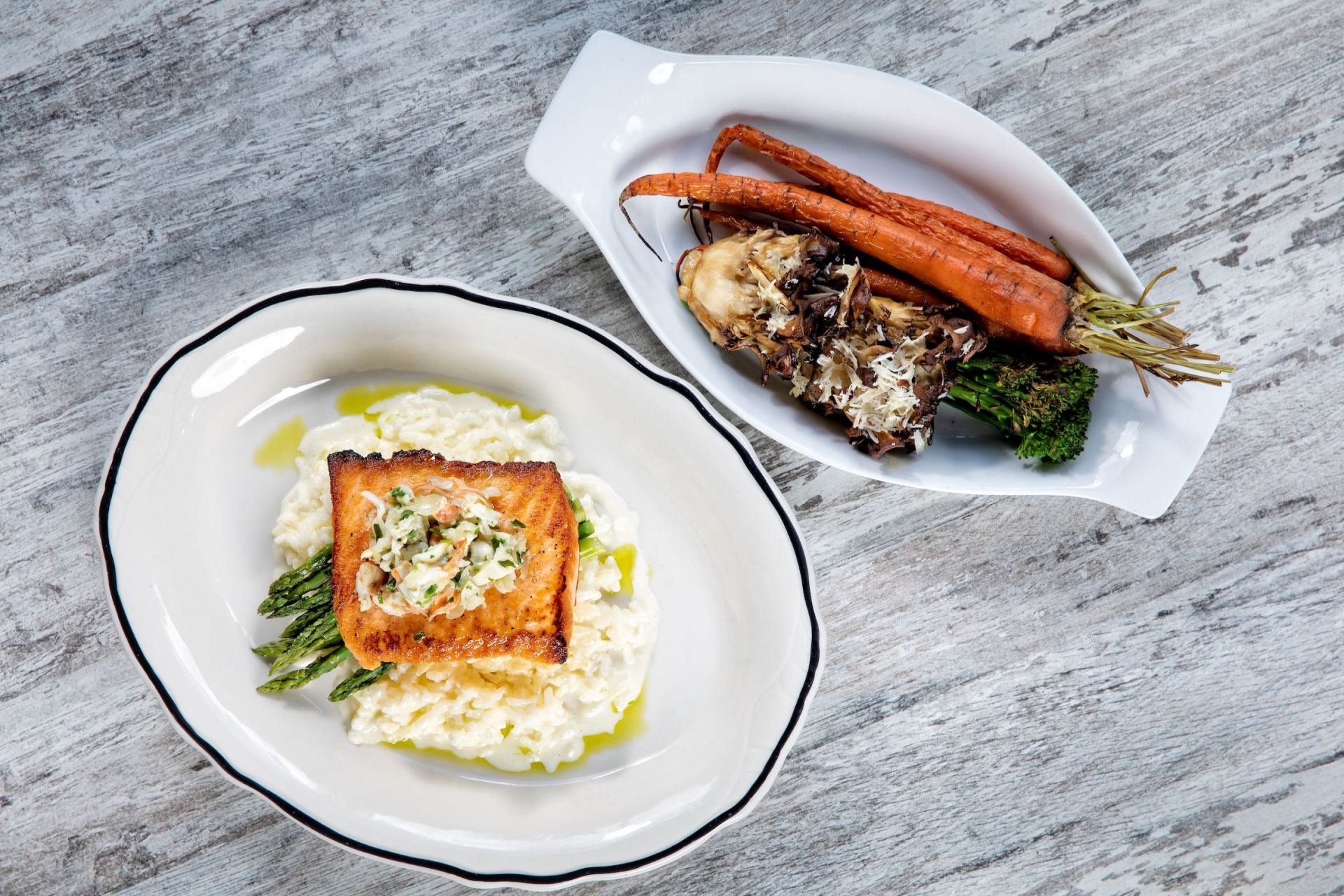 Two plated gourmet dishes with vegetables on a light gray table.