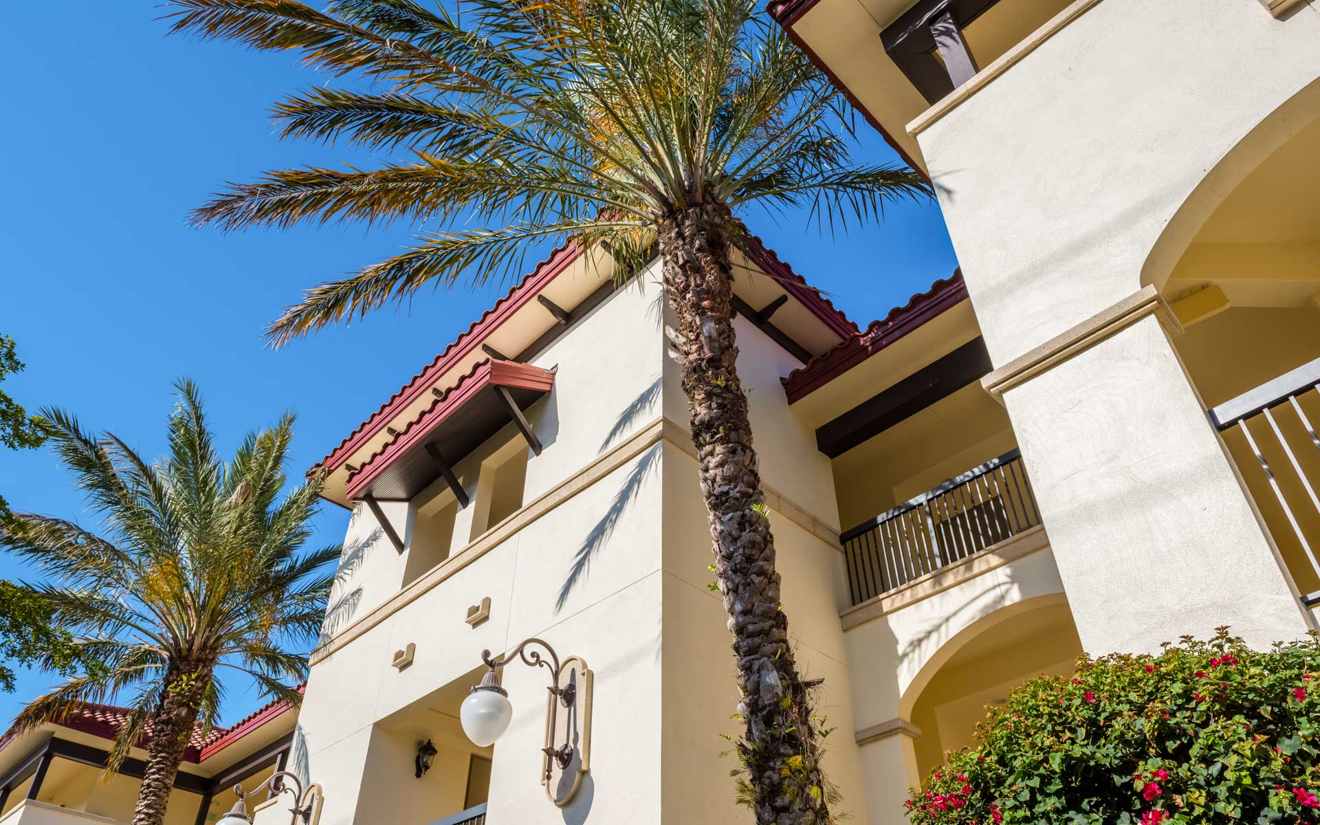 Sunlit Mediterranean-style apartment building with palm trees against a blue sky