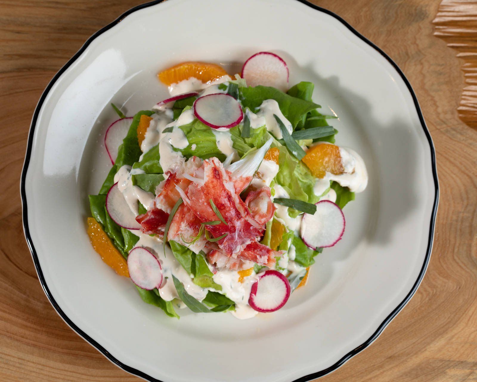 Fresh salad with radishes, greens, orange slices, and cheese on a white plate