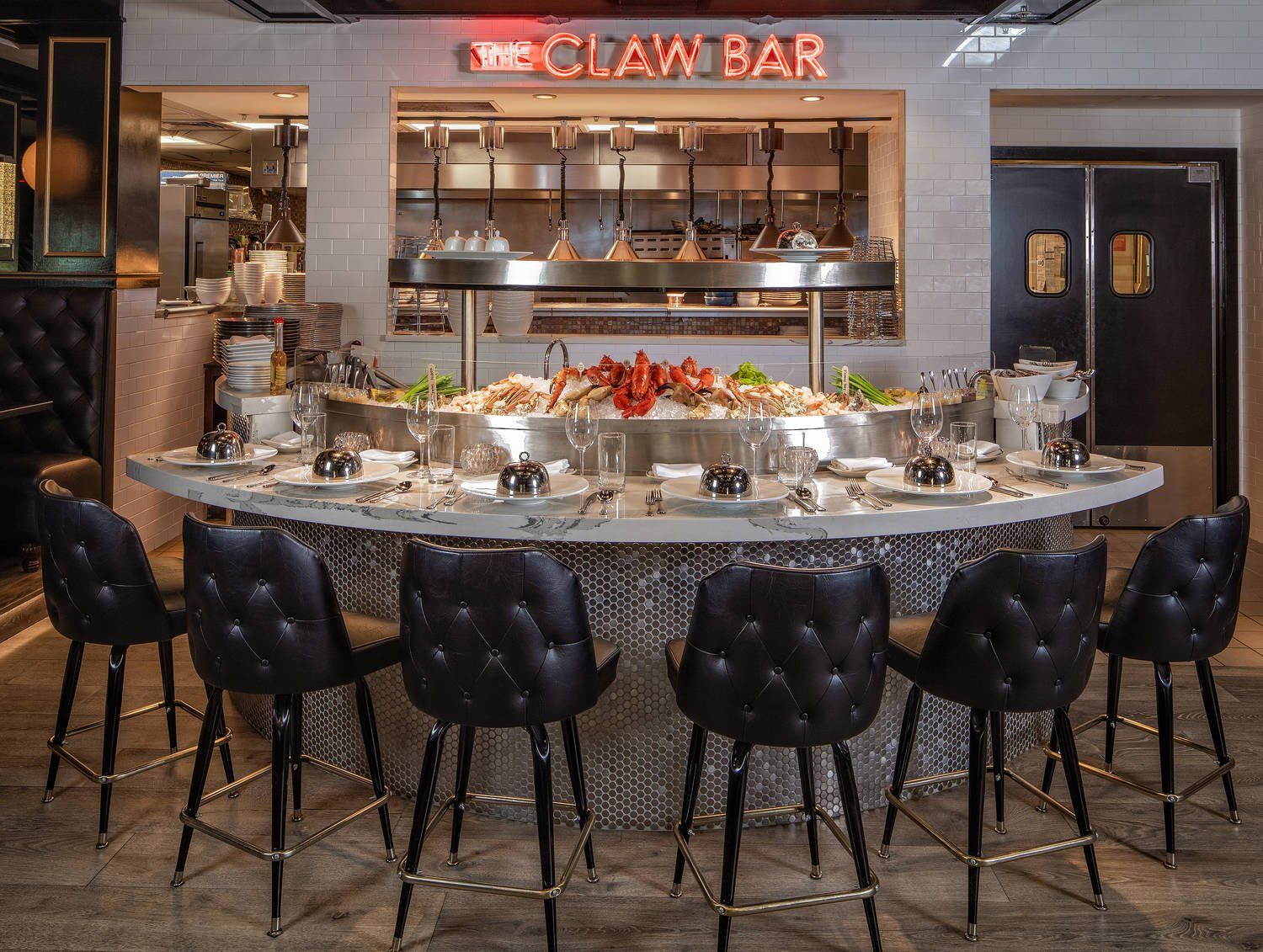 Modern bar interior with a curved marble counter, black stools, hanging lights, and a neon sign.