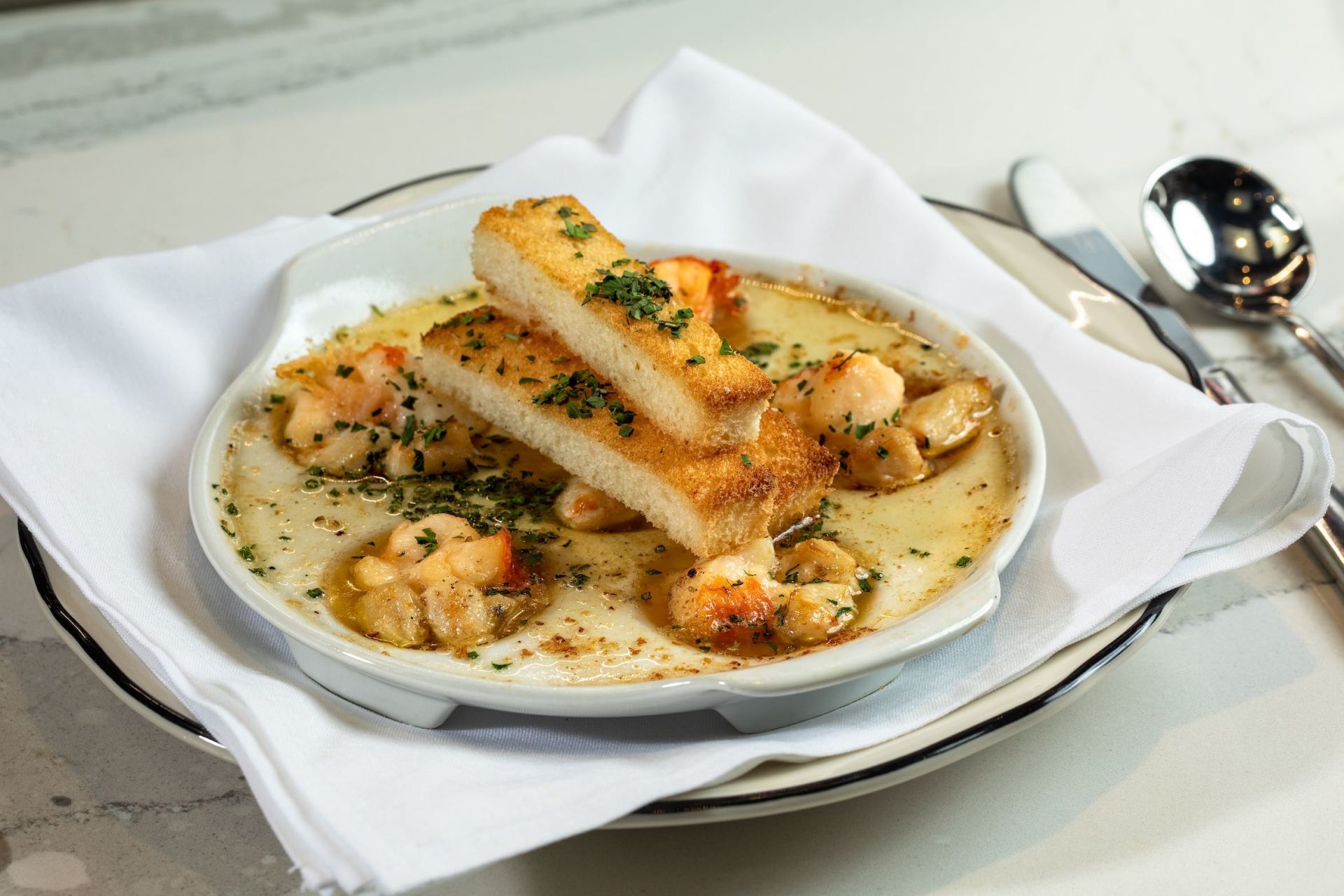Creamy seafood soup with breadsticks in a white bowl on a table setting