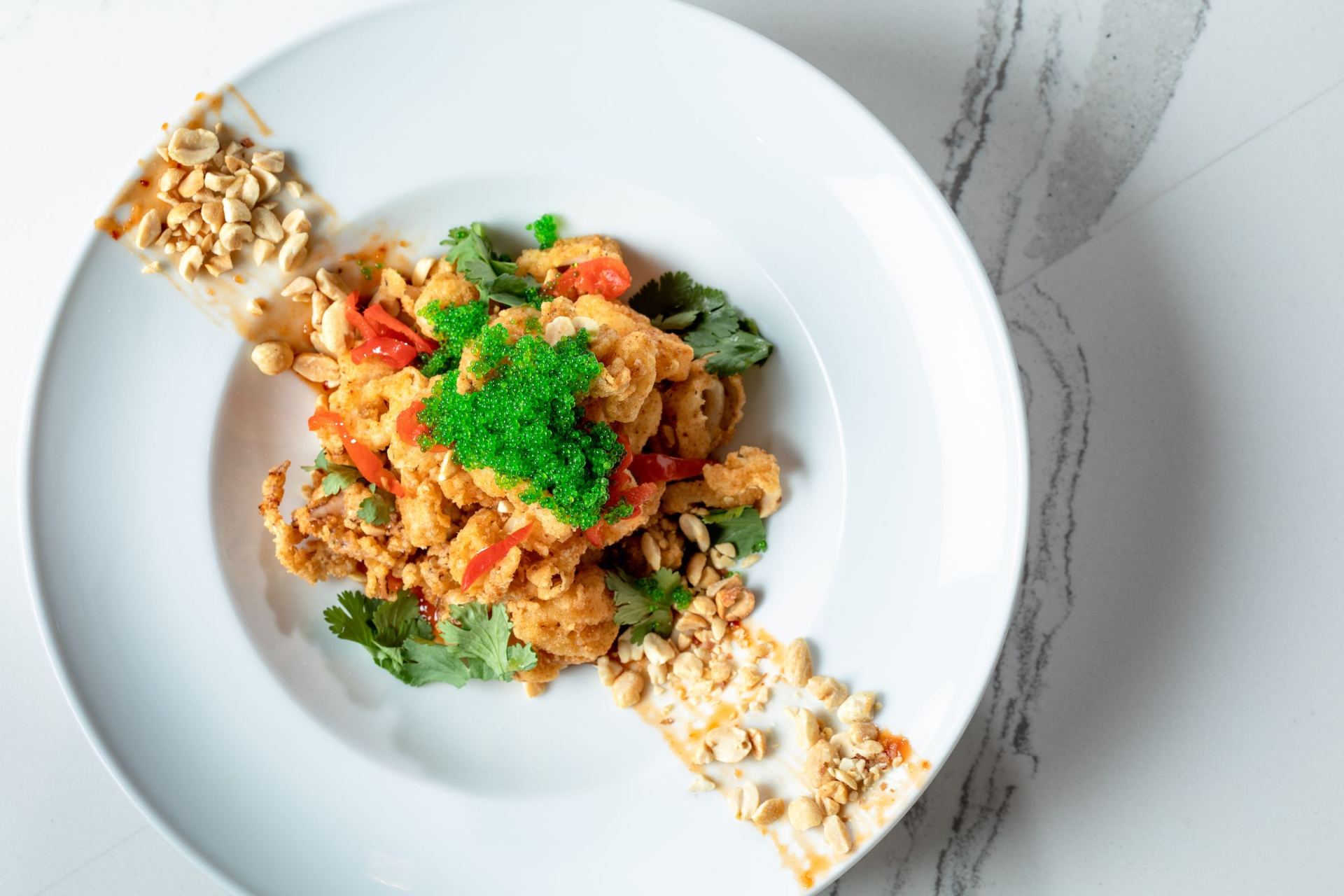 White plate with a colorful rice dish topped with green herbs, on a light marble surface