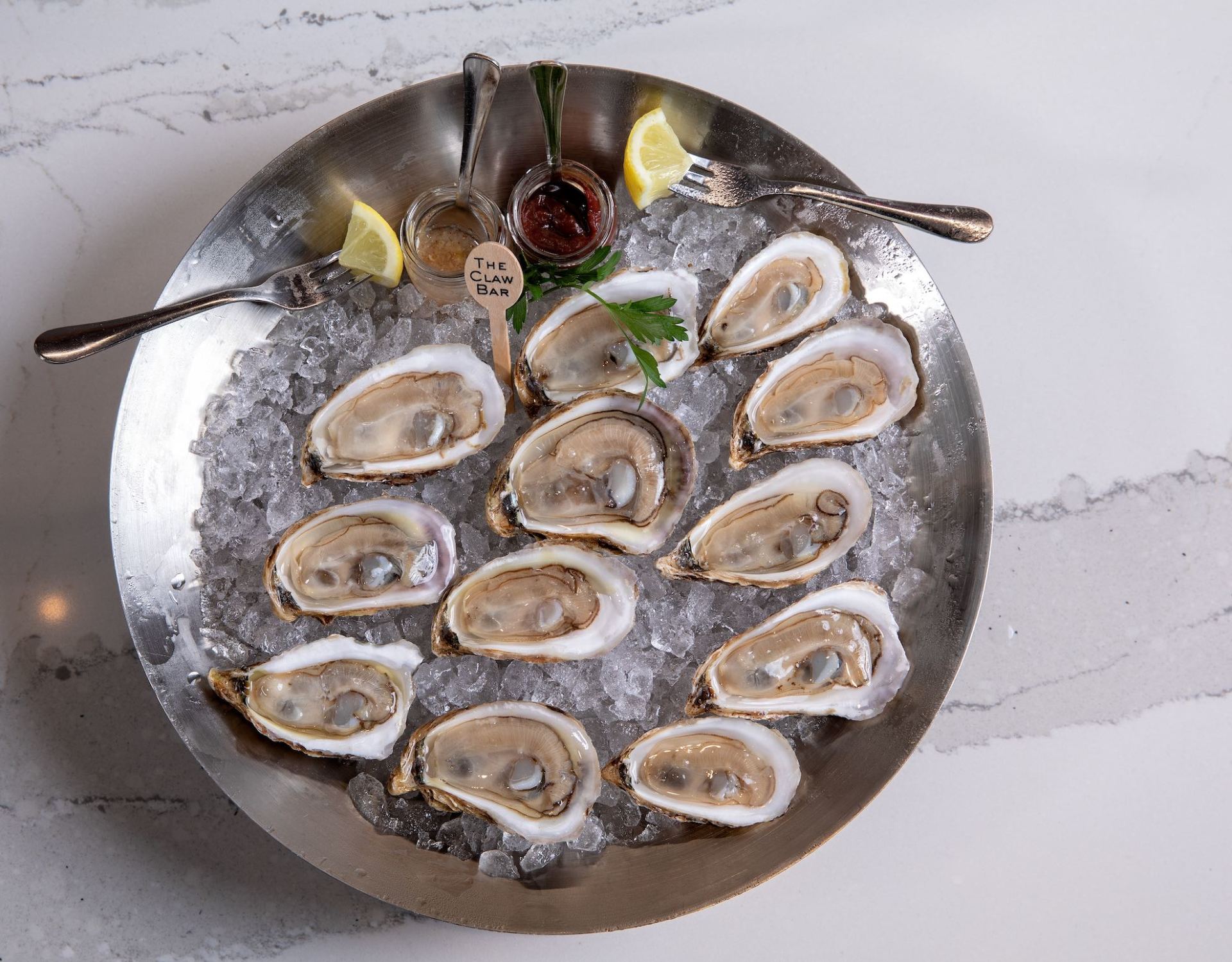 Plate of raw oysters on ice with lemon wedges and cocktail sauce on a silver tray