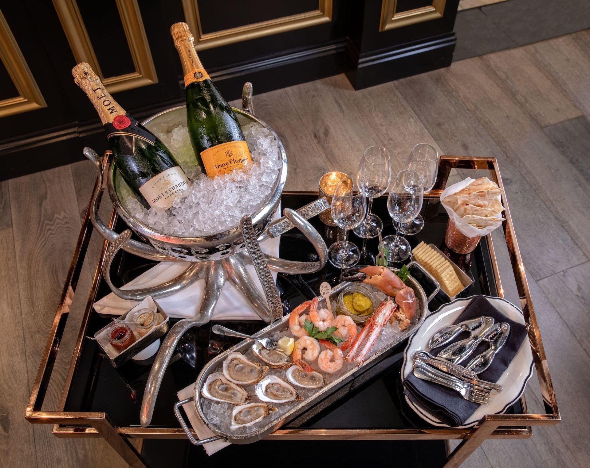 Tray with champagne bottles, oysters, shrimp platter, and glasses on a table at an elegant gathering