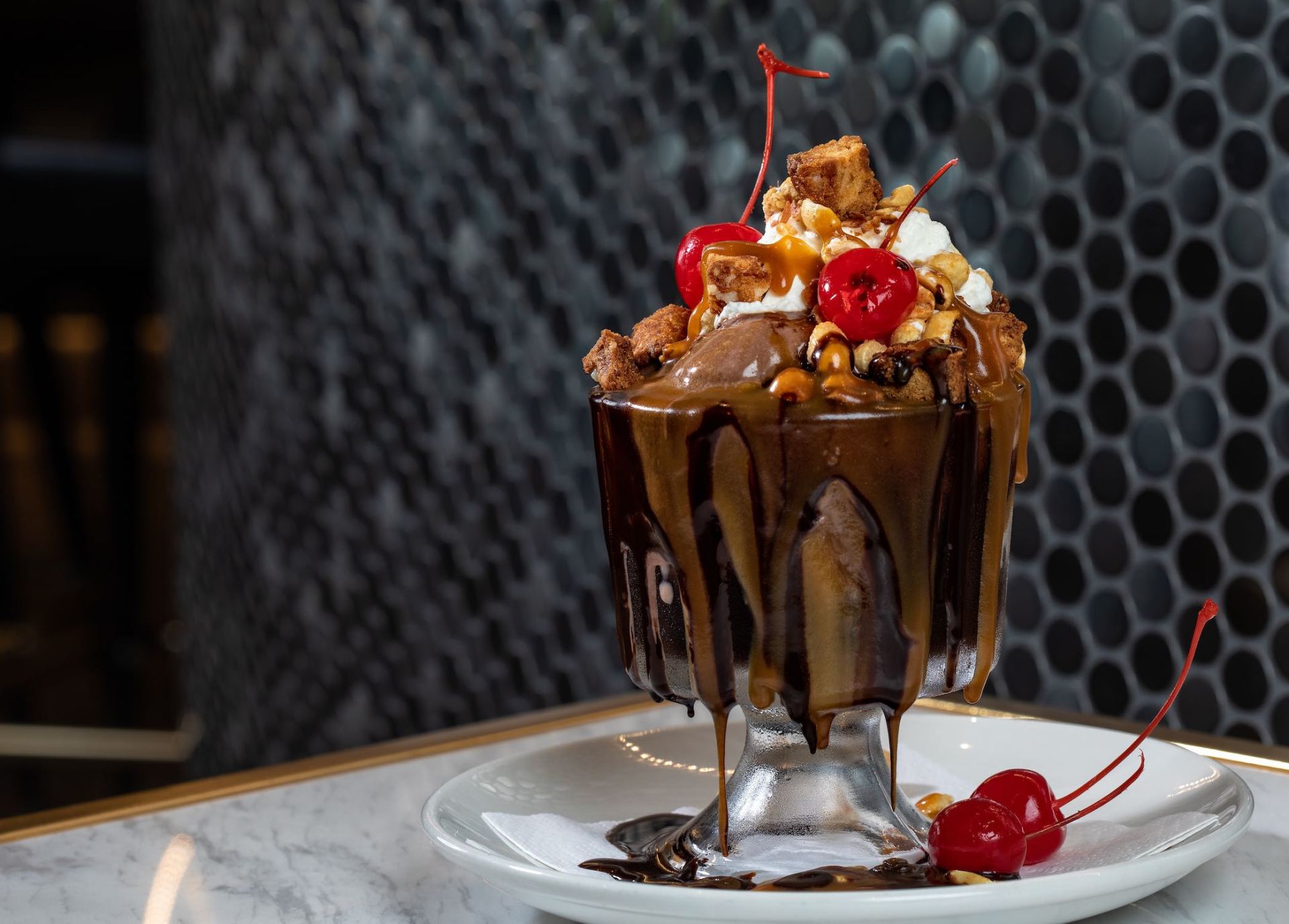 Chocolate sundae topped with whipped cream, cherries, and nuts on a white plate and saucer
