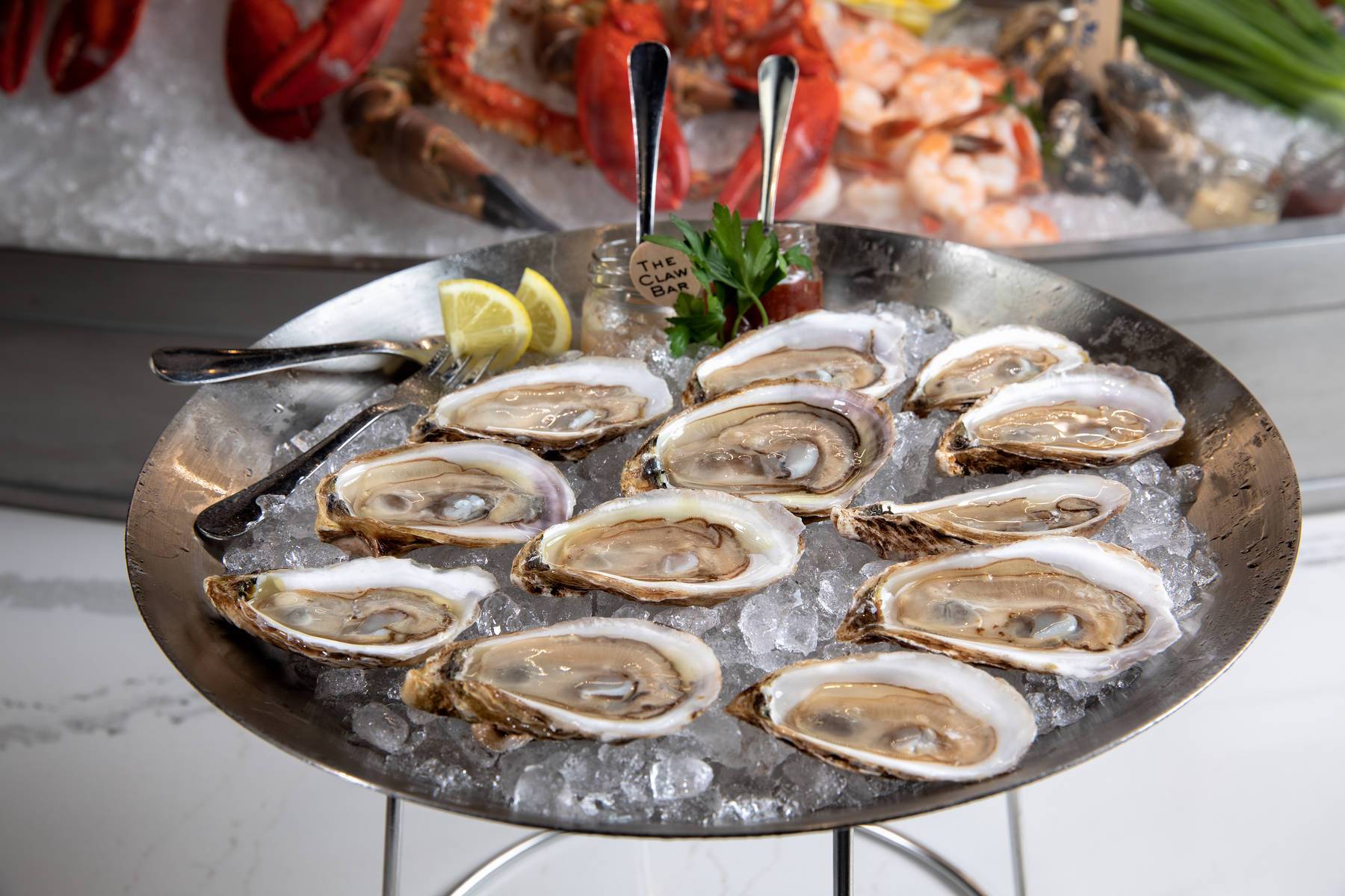Tray of raw oysters on ice with lemon wedges and parsley garnish at a seafood display
