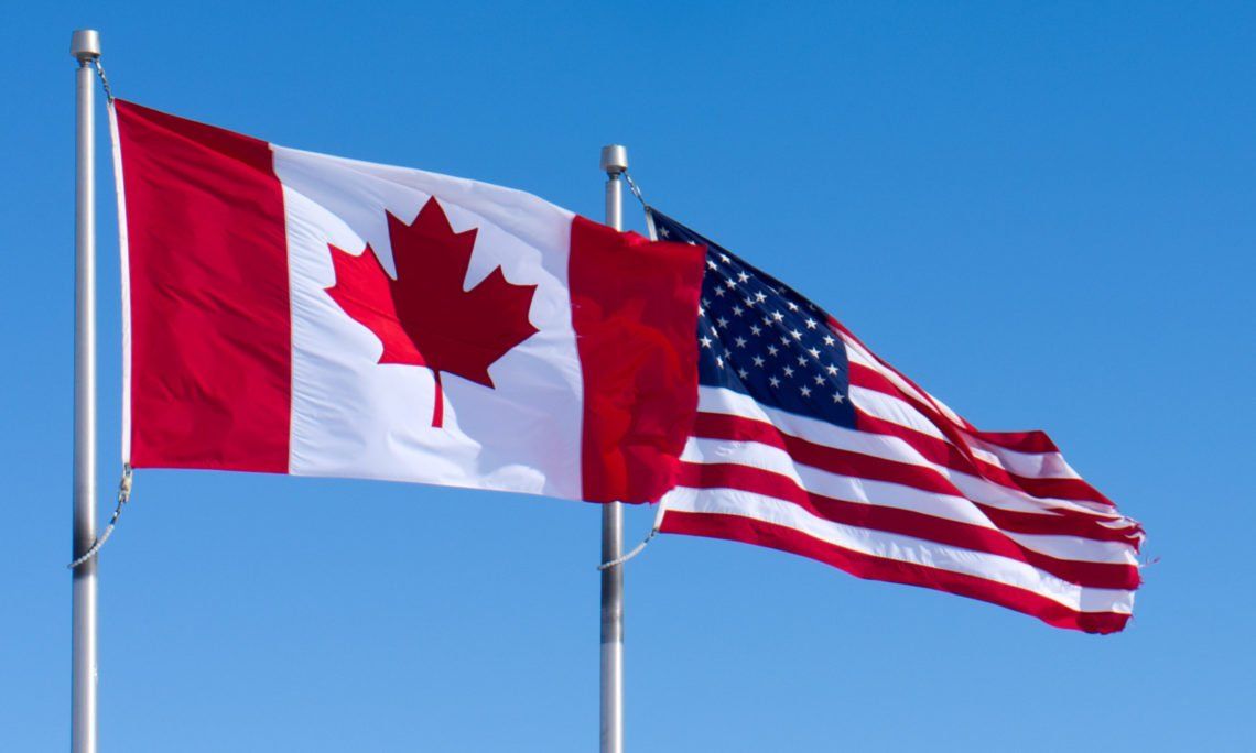 A canadian flag and an american flag are waving in the wind